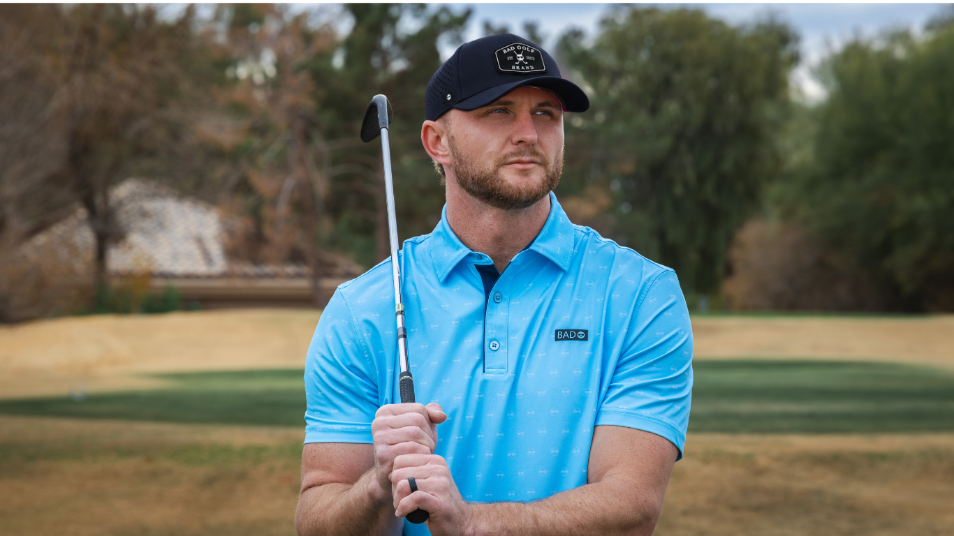 A man on a golf course wearing a bright blue polo shirt and a black cap, holding a golf club.